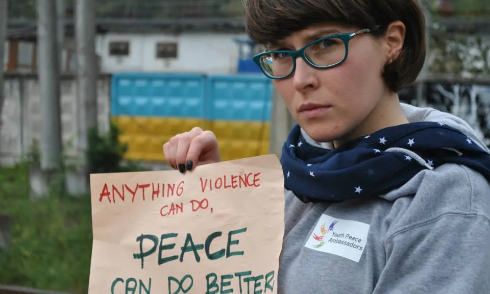 Aga Stajer amb un cartell que diu en anglès: Qualsevol cosa que pugui fer la violència, la pau la pot fer millor